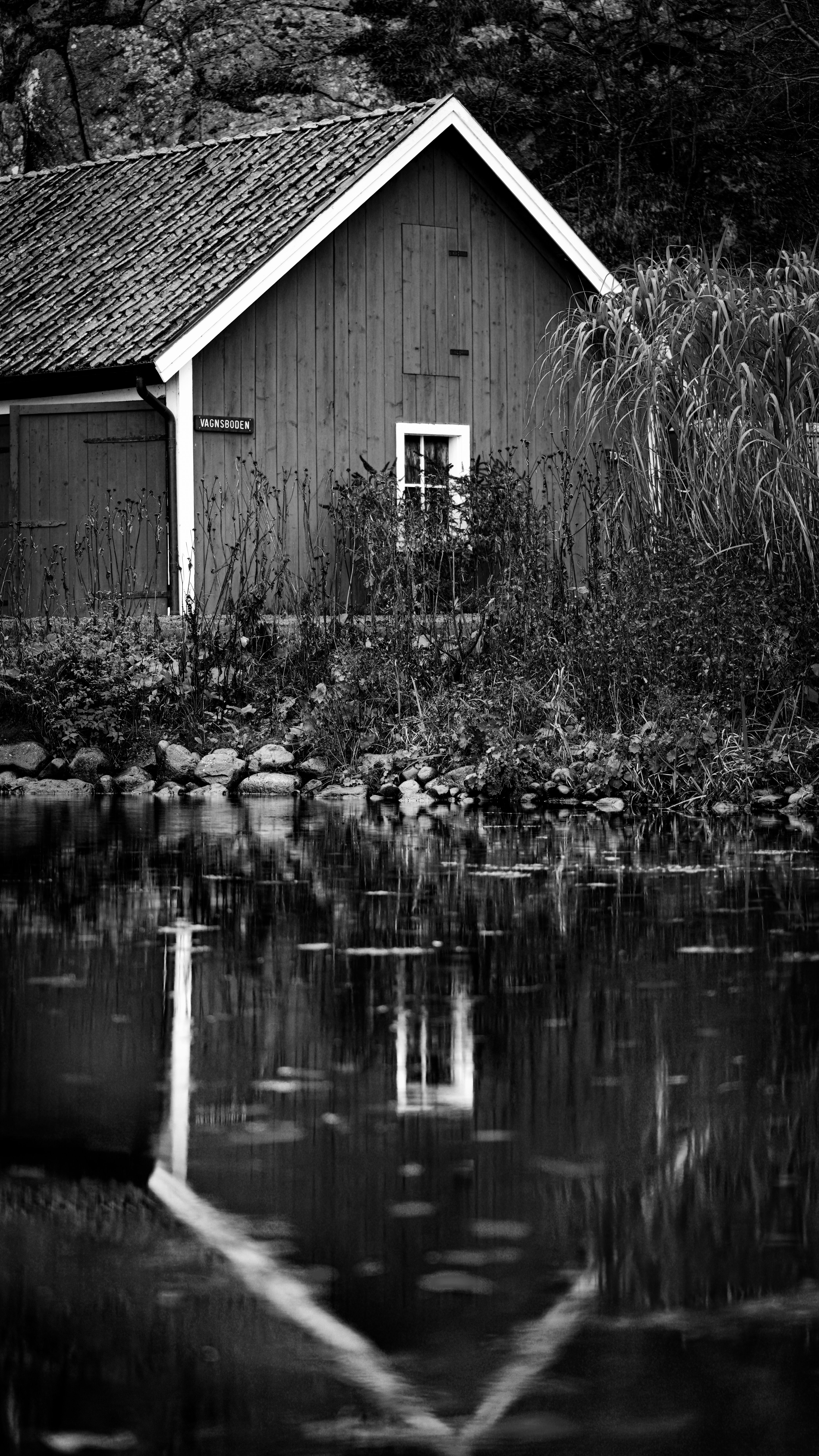 Rustic cabin reflected in a tranquil pond, monochrome tones.