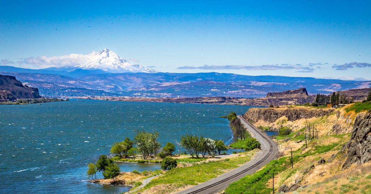 Breathtaking view of the Columbia River and Mount Hood with a winding railway along the shore.
