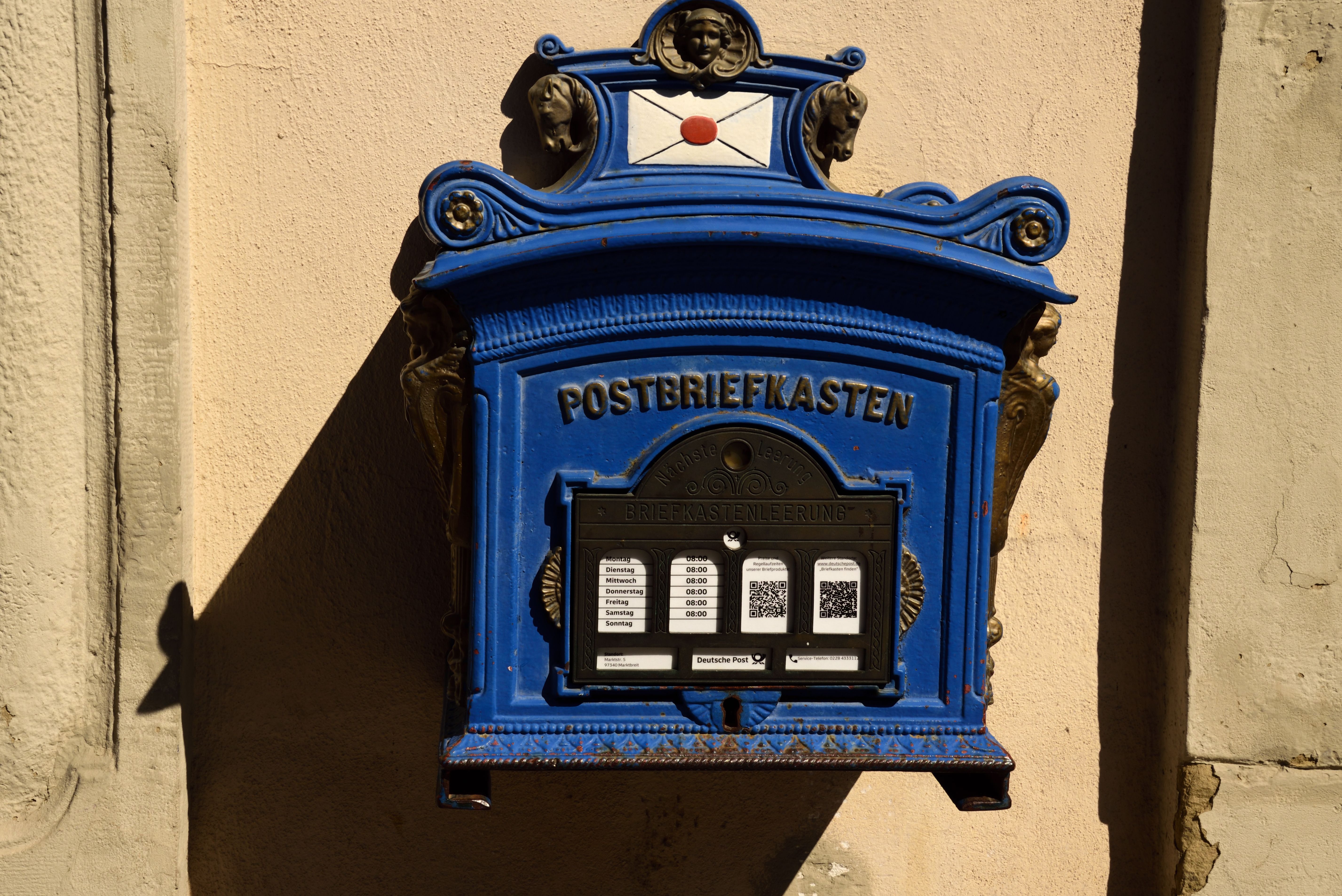 A vintage blue mailbox in Marktbreit, Germany, showing intricate designs and postal hours.