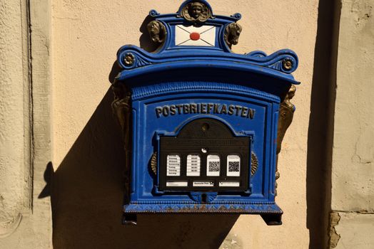A vintage blue mailbox in Marktbreit, Germany, showing intricate designs and postal hours.