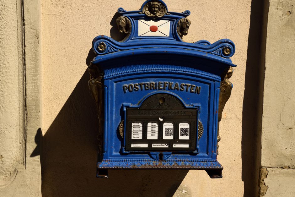 A vintage blue mailbox in Marktbreit, Germany, showing intricate designs and postal hours.