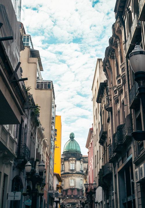 Free View of a historic street with classical architecture, leading to a dome building under a partly cloudy sky. Stock Photo