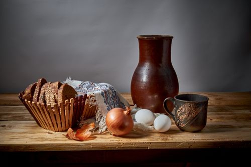 Free A rustic still life featuring bread, onions, eggs, and earthenware on a wooden table. Stock Photo