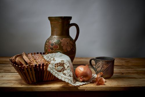 Free A still life composition featuring bread, onions, a ceramic jug, and a mug on a wooden table. Stock Photo