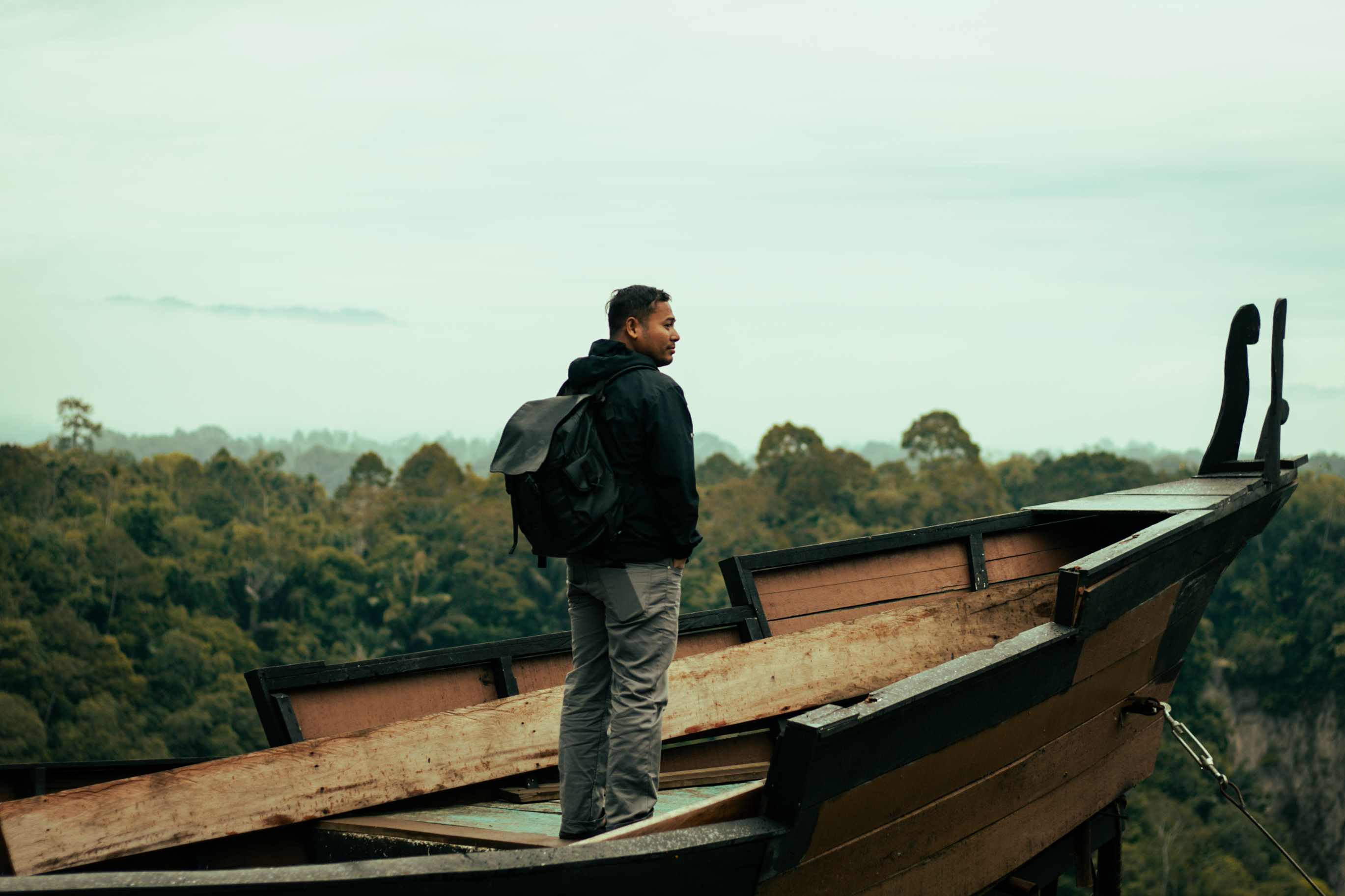 A traveler stands on a traditional boat overlooking the lush Padang landscape in West Sumatra, Indonesia.