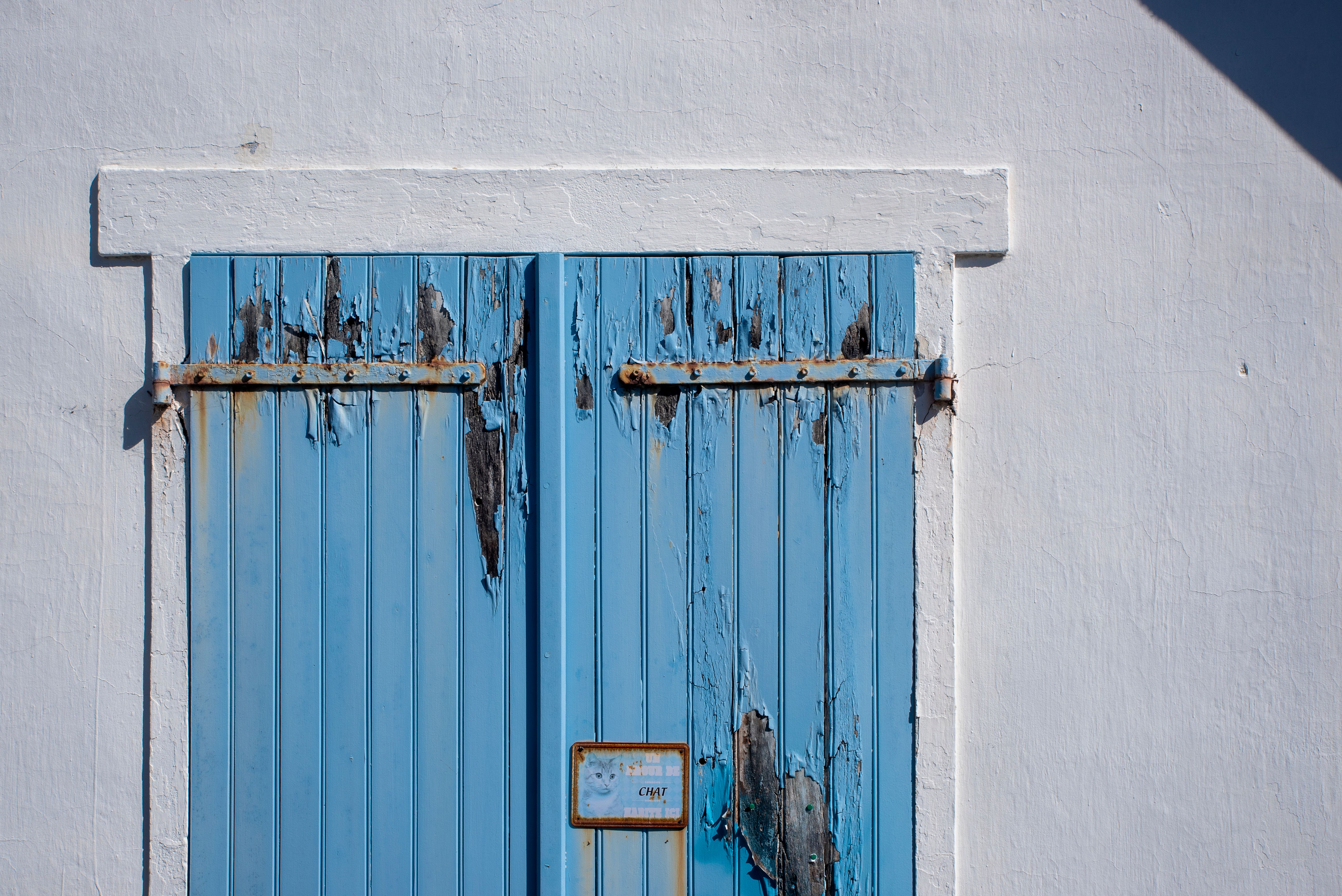 Old blue wooden shutters with peeling paint set on a white wall, displaying rustic charm.