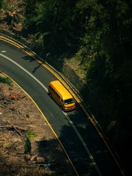 Aerial view of a yellow van driving on a winding road through a forest in Kuala Lumpur, Malaysia.