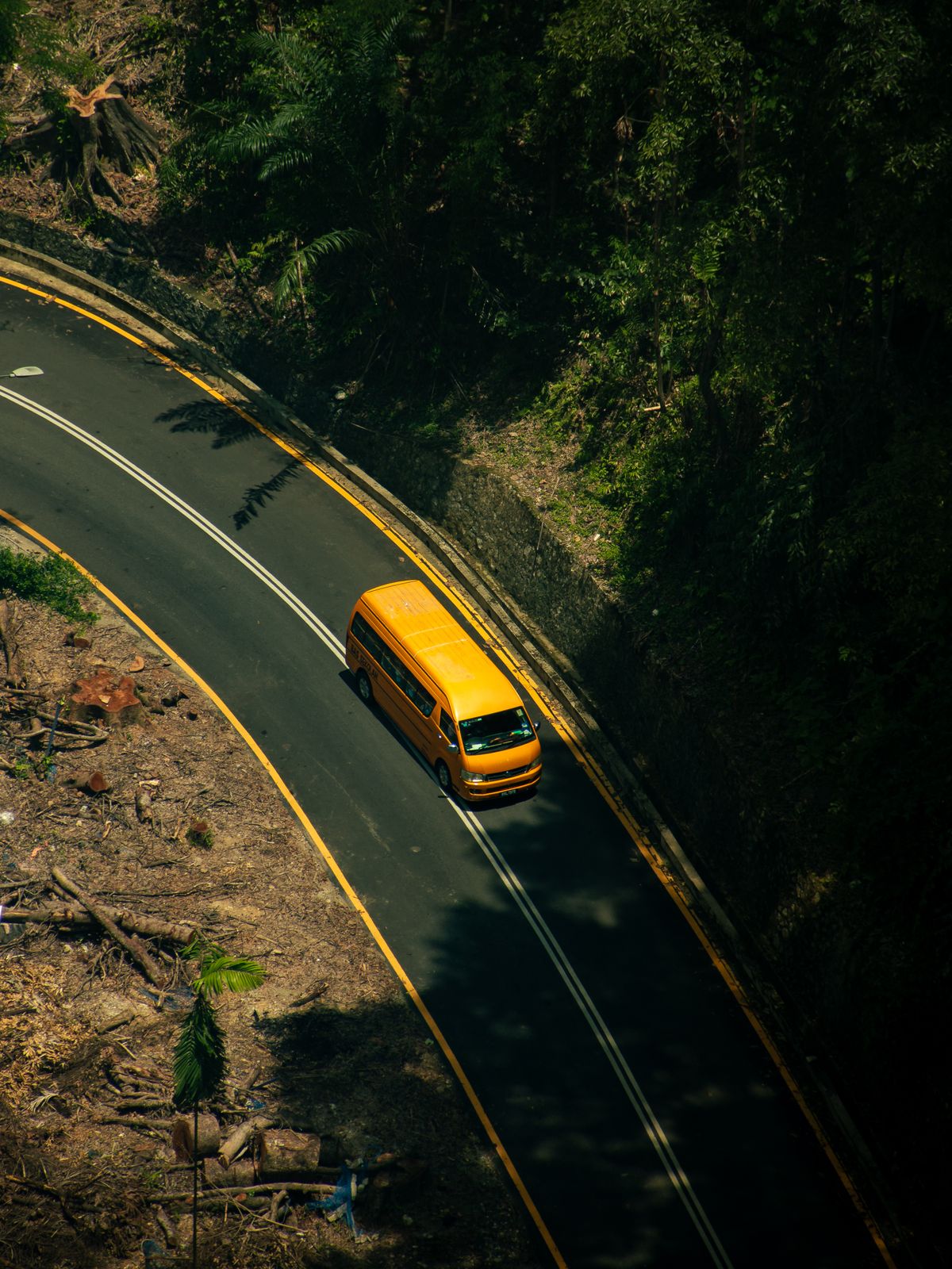 A yellow van driving a winding road near Kuala Lumpur, Malaysia — the flat side panel of a van is the area most worth branding