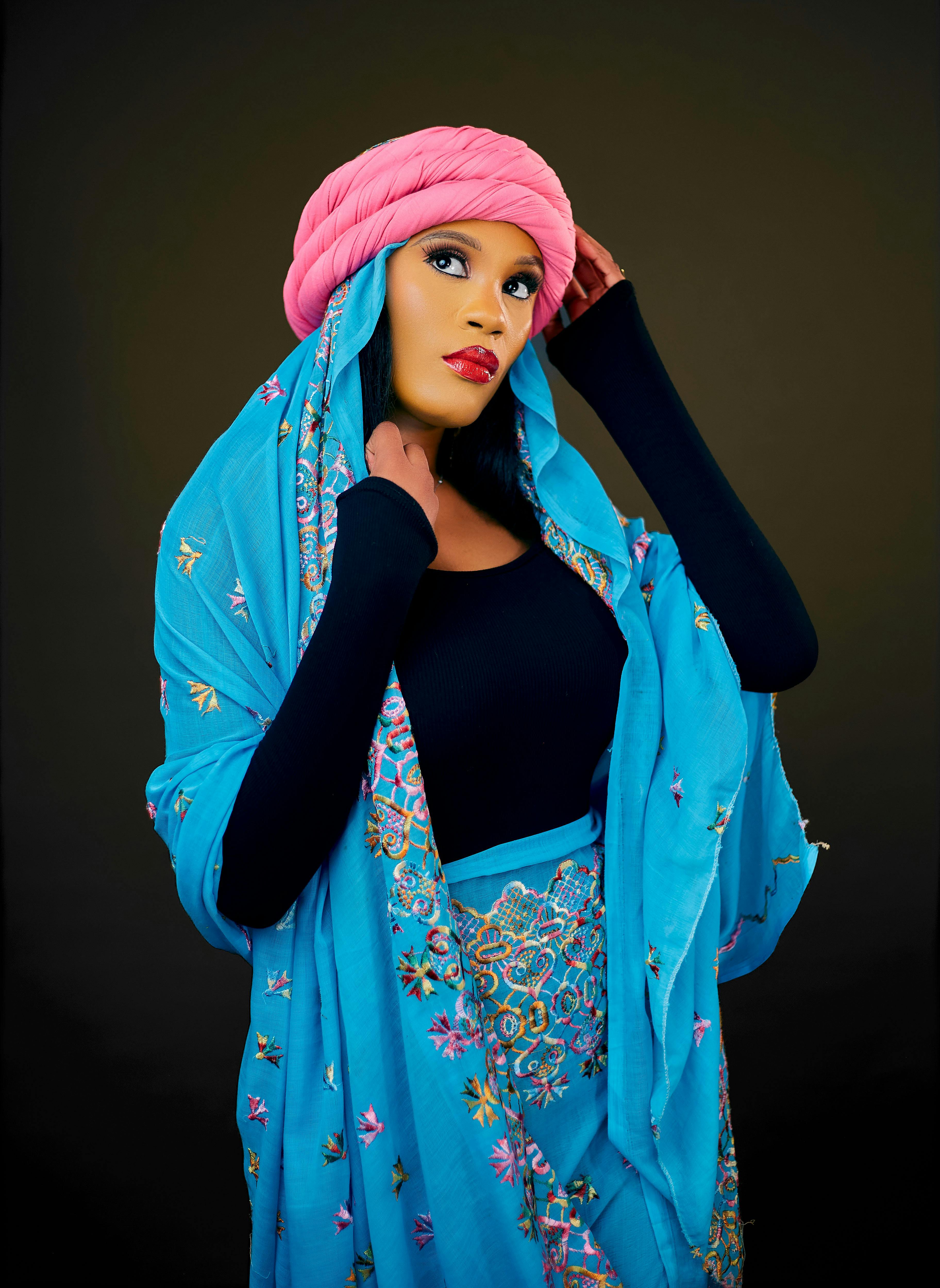 Portrait of a woman in traditional blue and pink attire on a dark background.