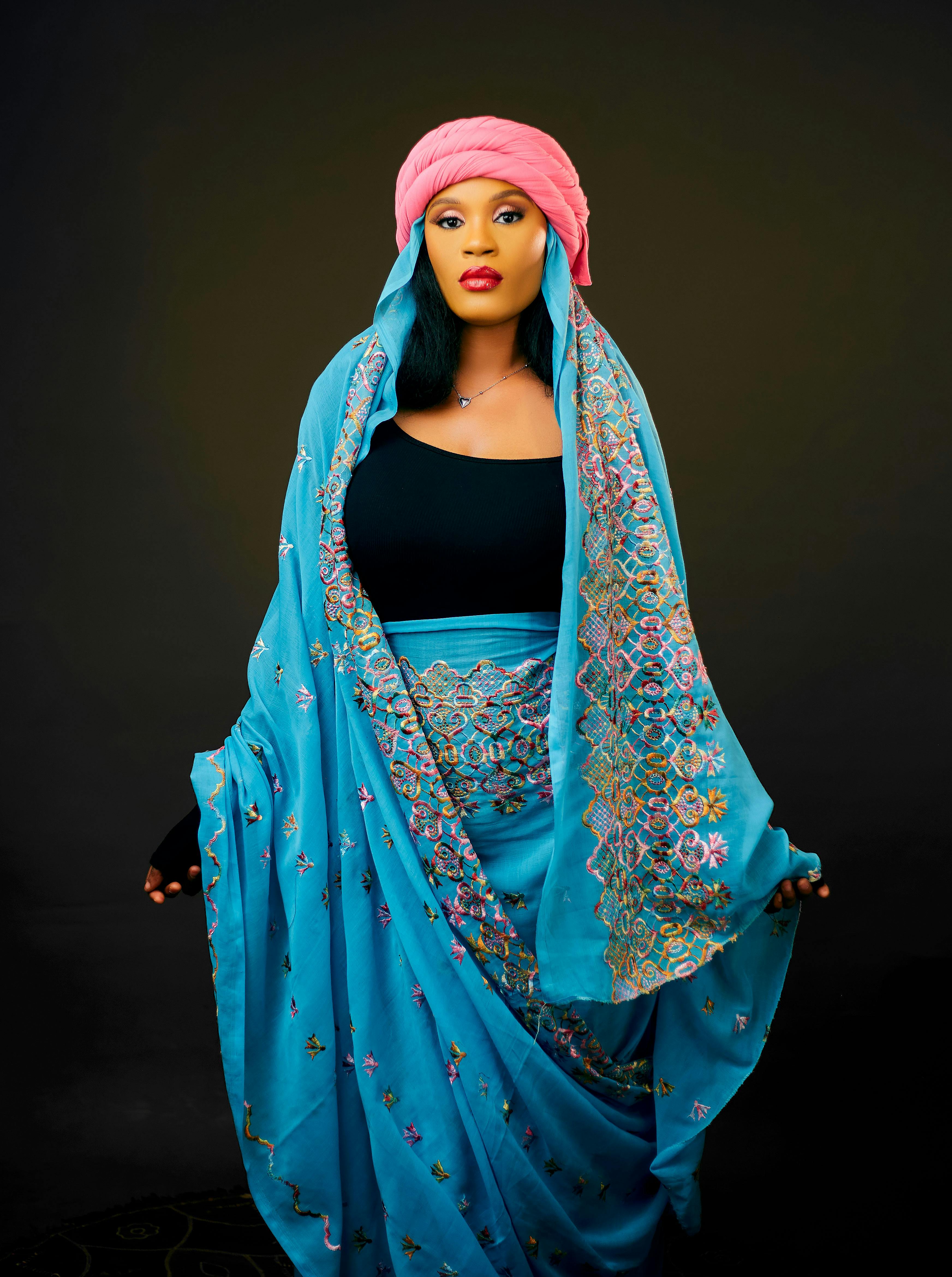 Portrait of woman in vibrant traditional attire with pink headscarf, elegant designs.