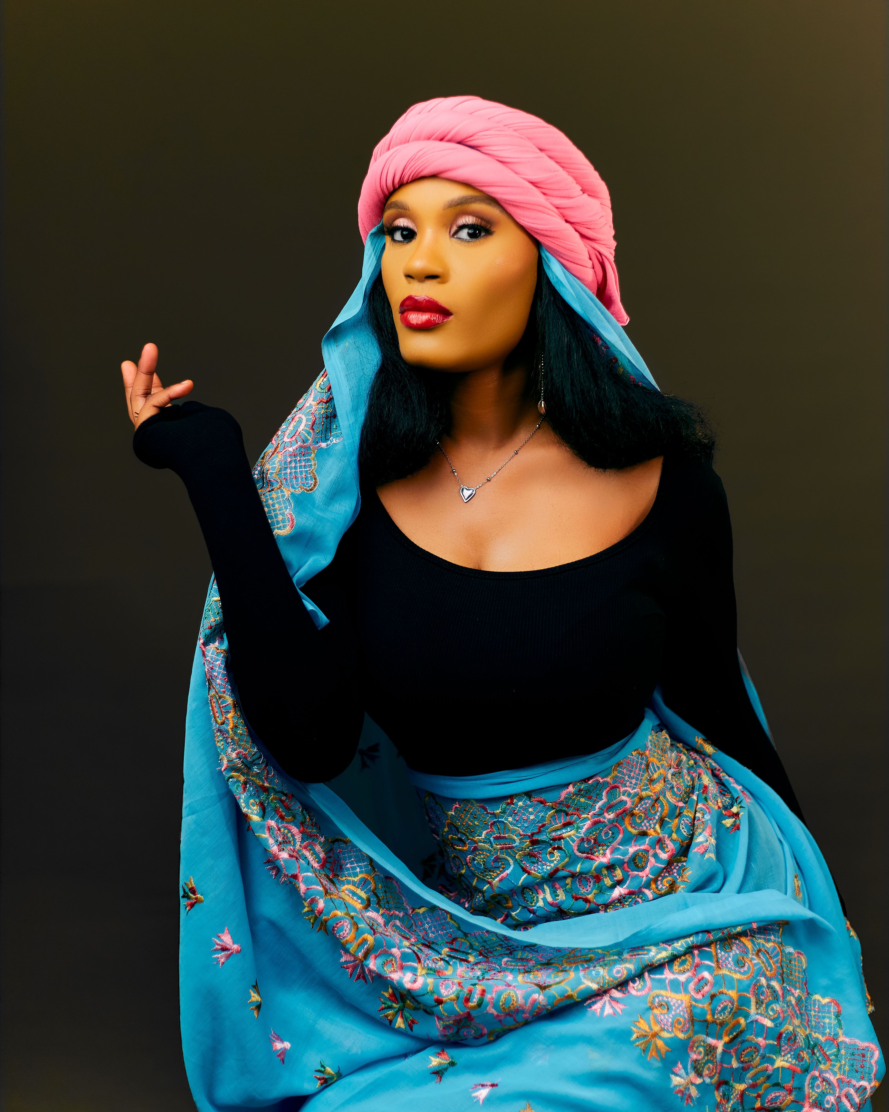 A woman poses gracefully in traditional attire with vivid colors and intricate patterns.