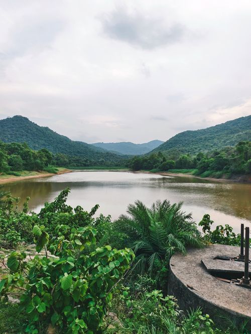 Free Tranquil lake surrounded by lush green hills and cloudy sky, capturing a peaceful natural environment. Stock Photo