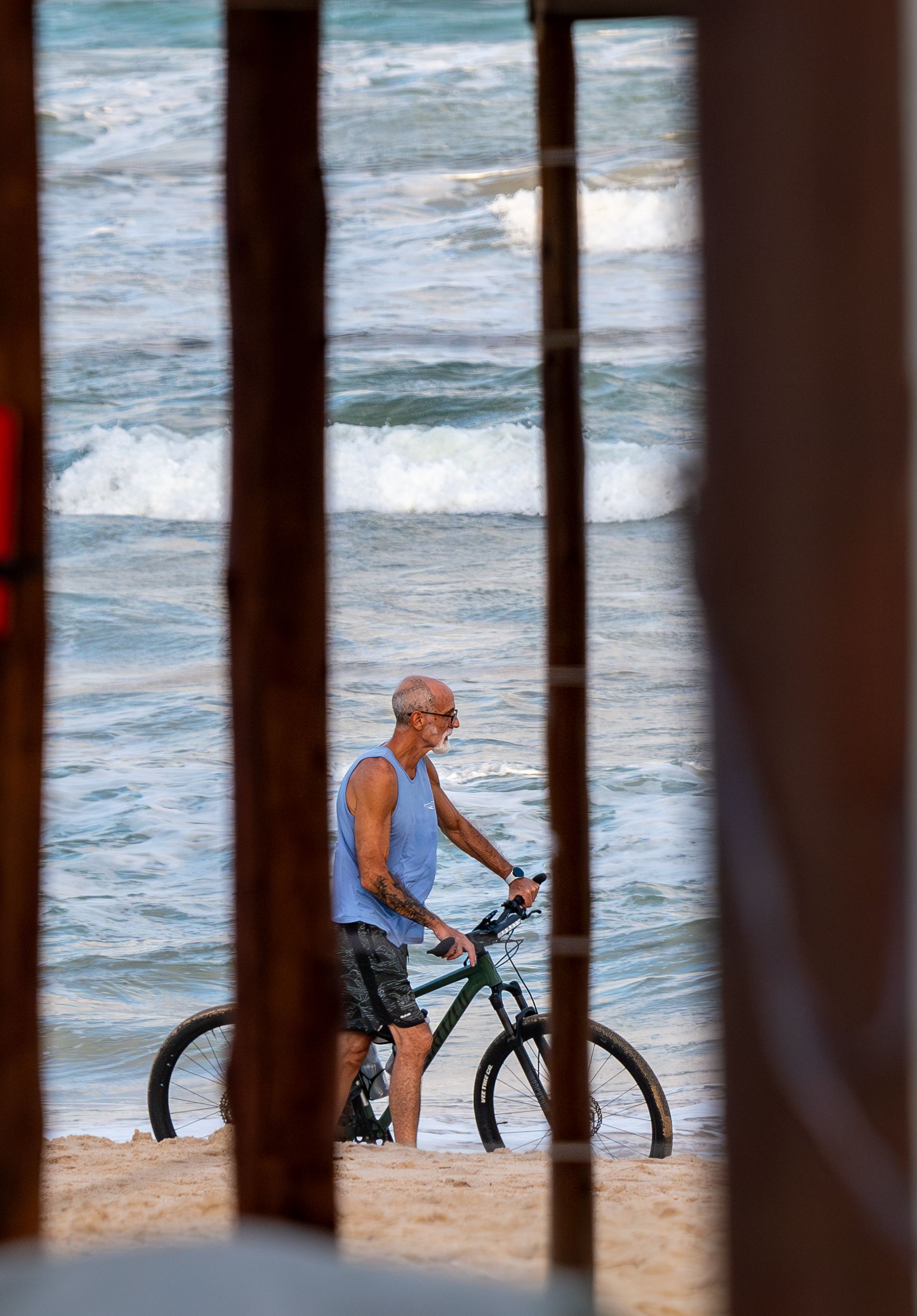 A senior adult walks his bicycle along Bahía beach, capturing a moment of peaceful seaside leisure.