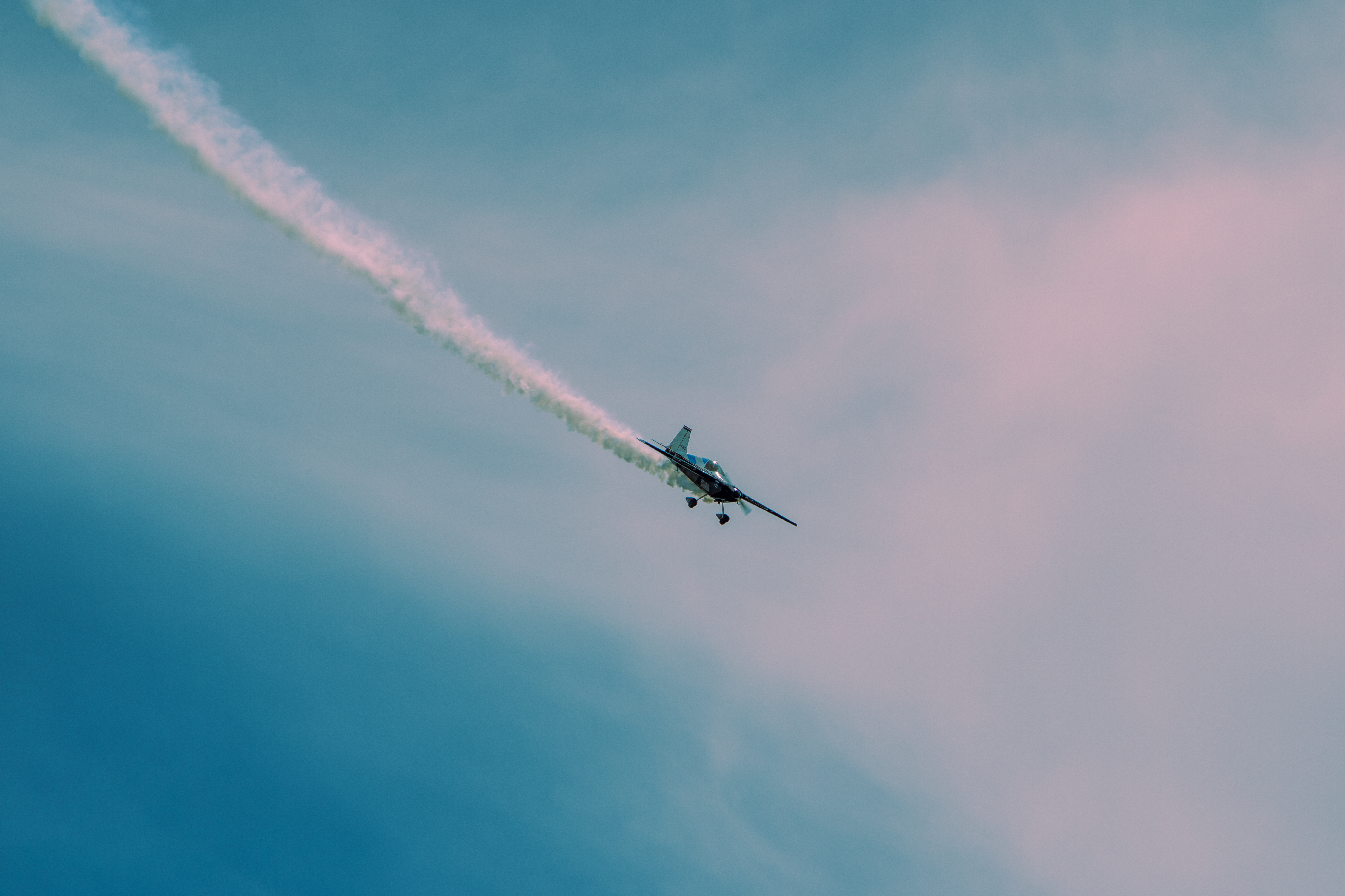 An aerobatic plane creating a smoke trail against the cloudy blue sky.