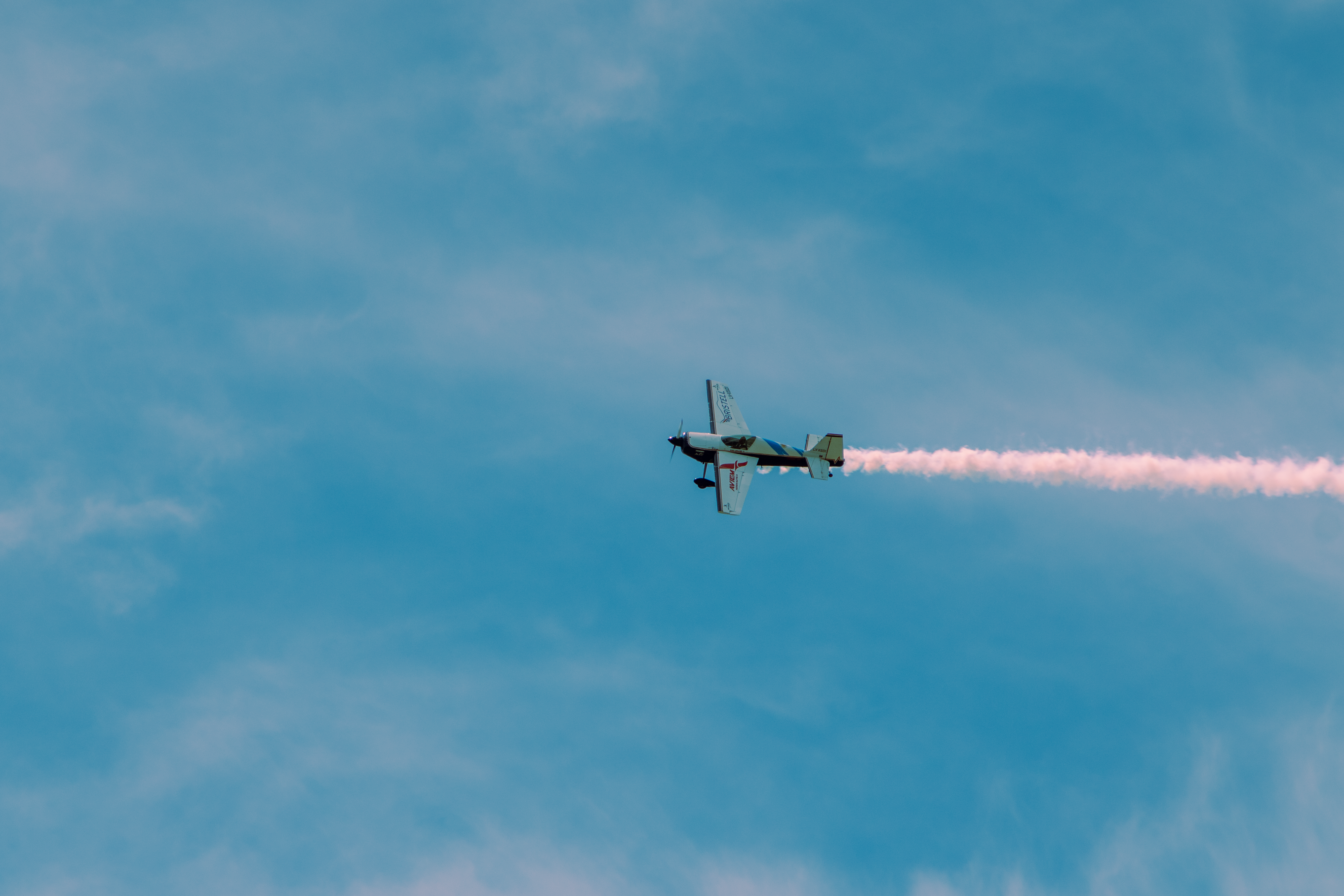 Dramatic shot of a stunt plane with smokestream against bright blue sky, performing aerobatic stunts.