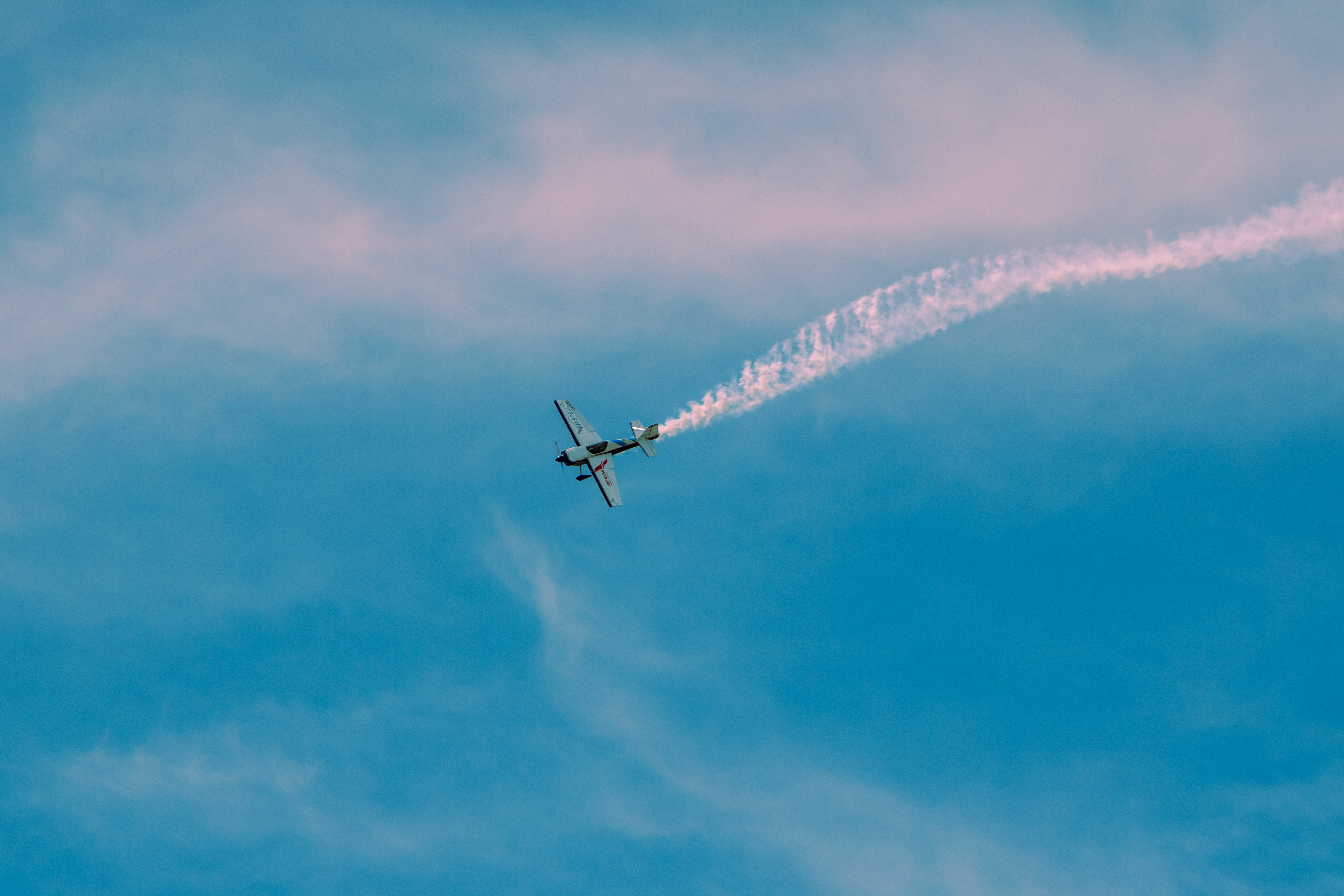 A stunning aerobatic plane performs stunts with a smoke trail in a clear blue sky.