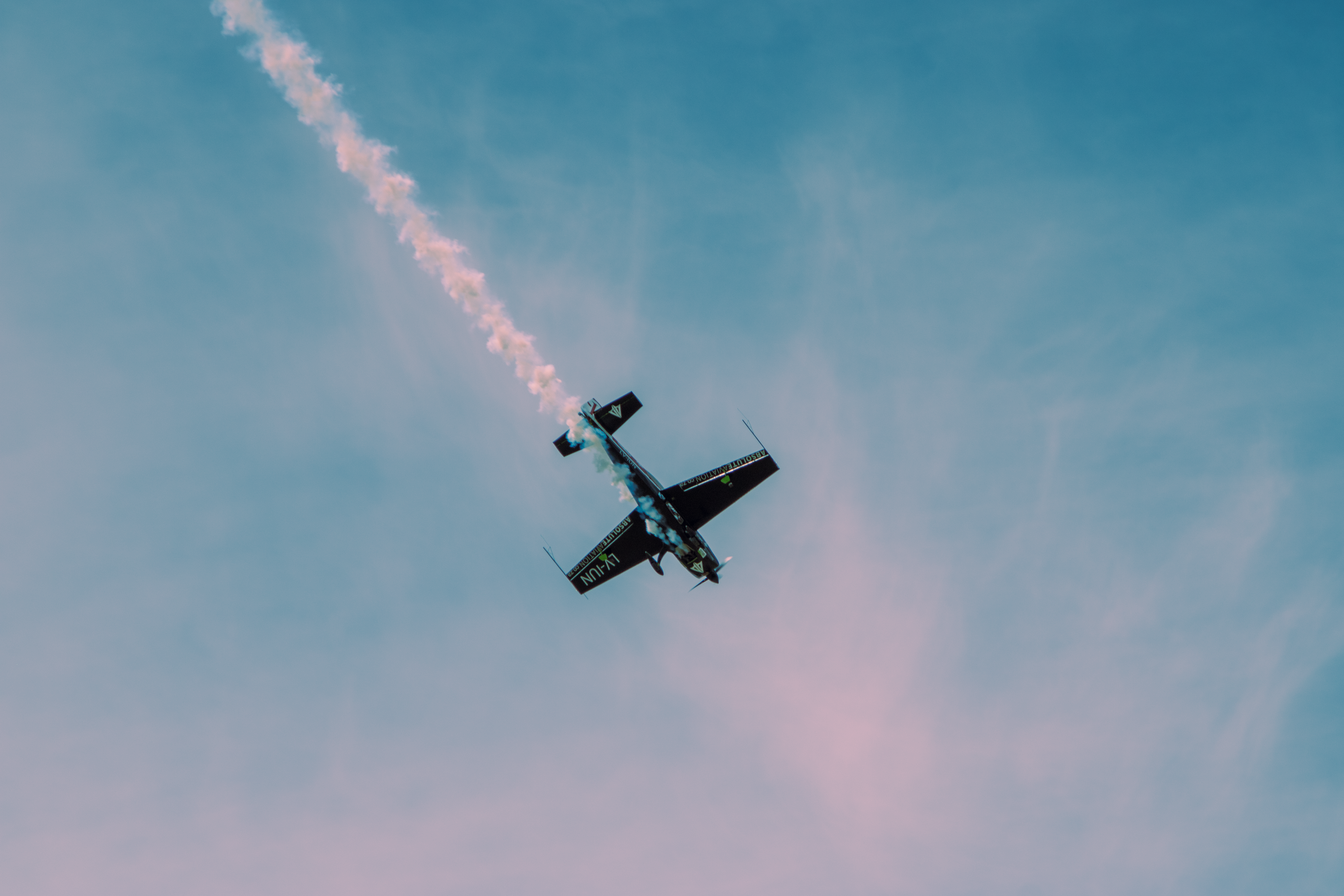 Dramatic stunt airplane showcasing aerobatics with a smoke trail against a clear sky.