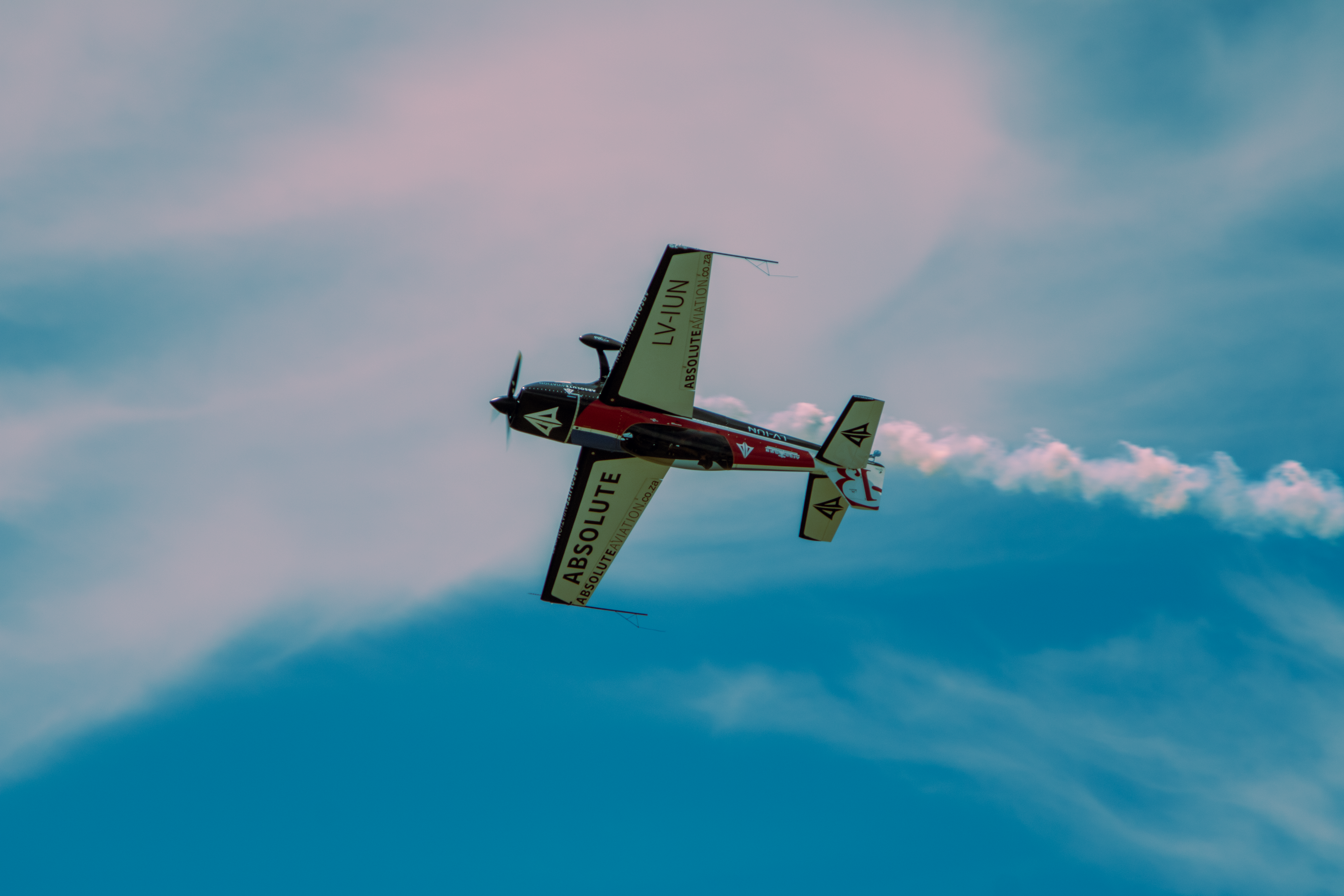 An aerobatic plane performing a smoke stunt against a bright blue sky.