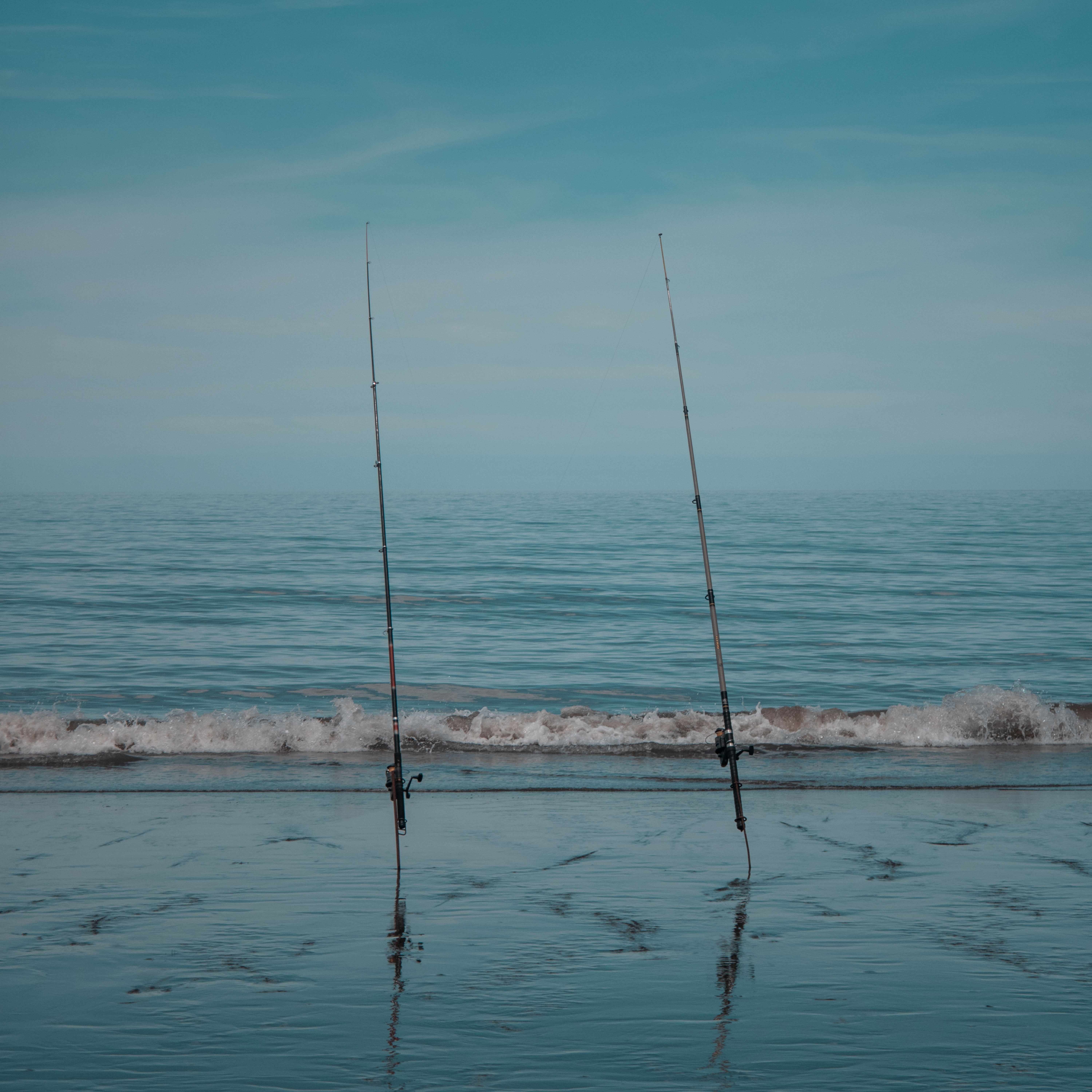 Peaceful beach scene featuring two fishing rods by the shore under a calm sky.