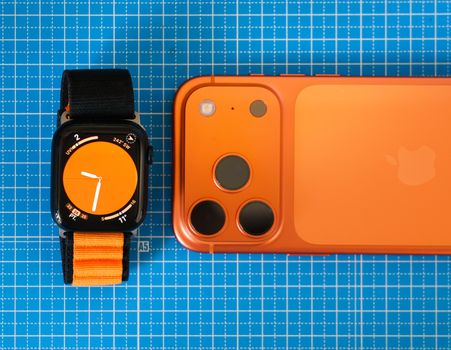Minimalist setup featuring an orange-themed smartphone and smartwatch on a blue grid background.