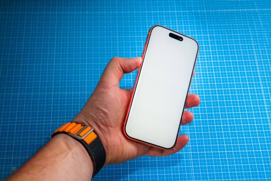 Hand holding a modern smartphone with a blank screen over a blue grid background.