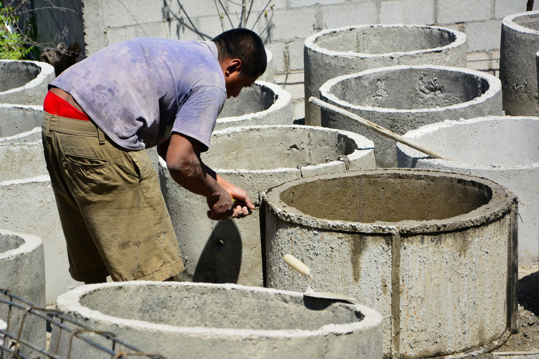 A worker repairs concrete structures outside under the sun, showcasing manual labor.