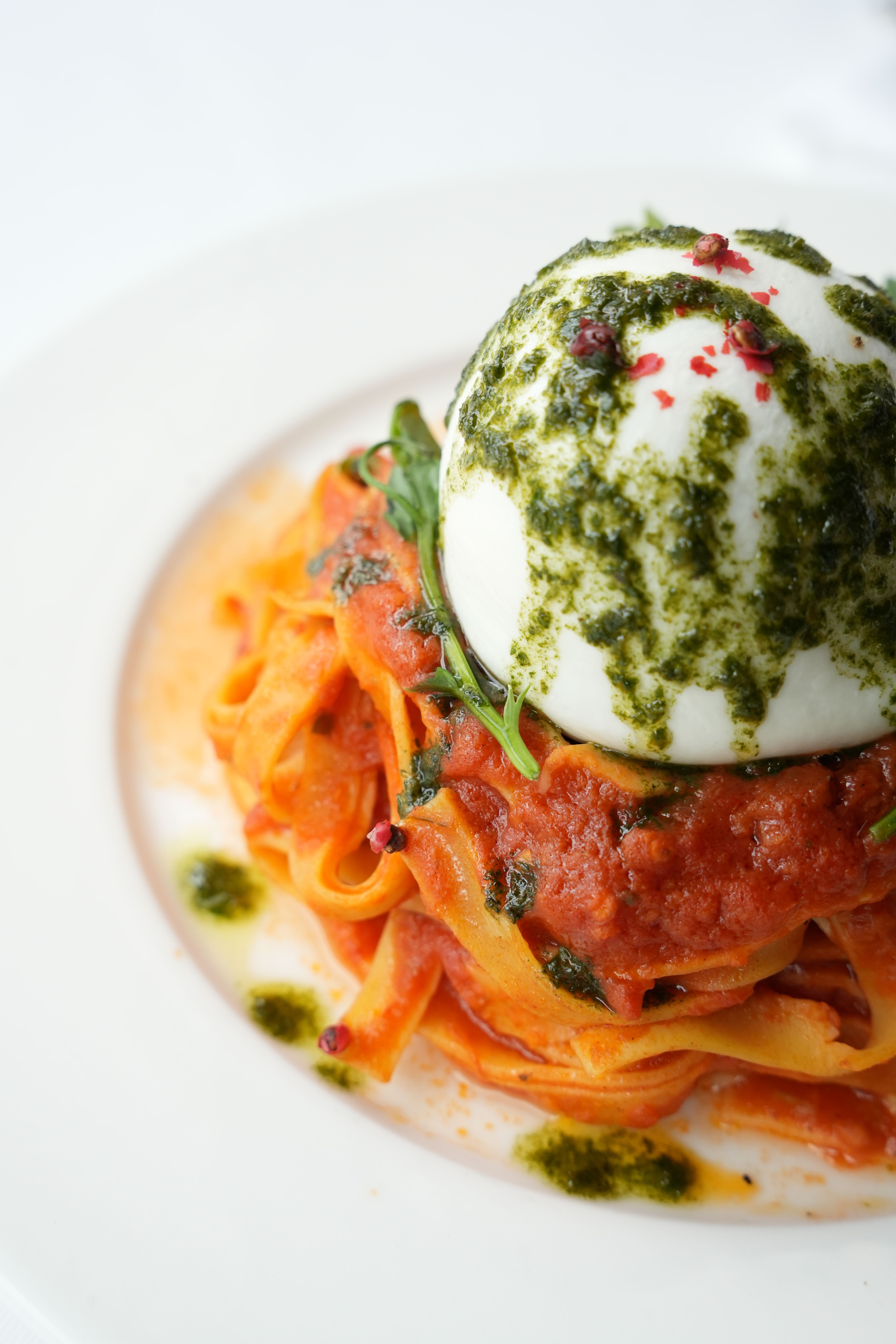 A gourmet burrata cheese atop fresh tomato pasta with pesto sauce.
