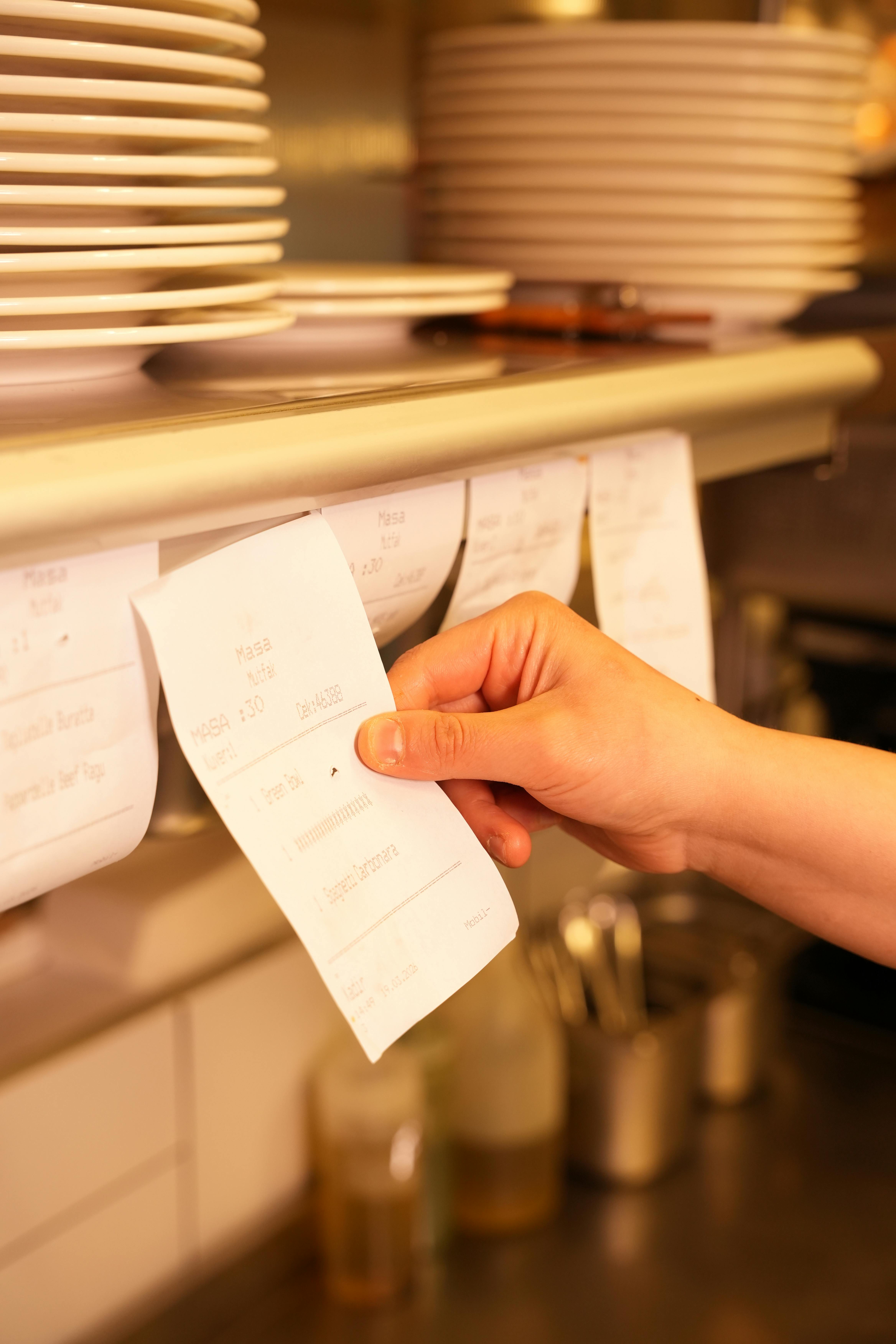 Hand managing order tickets in a busy restaurant kitchen environment.