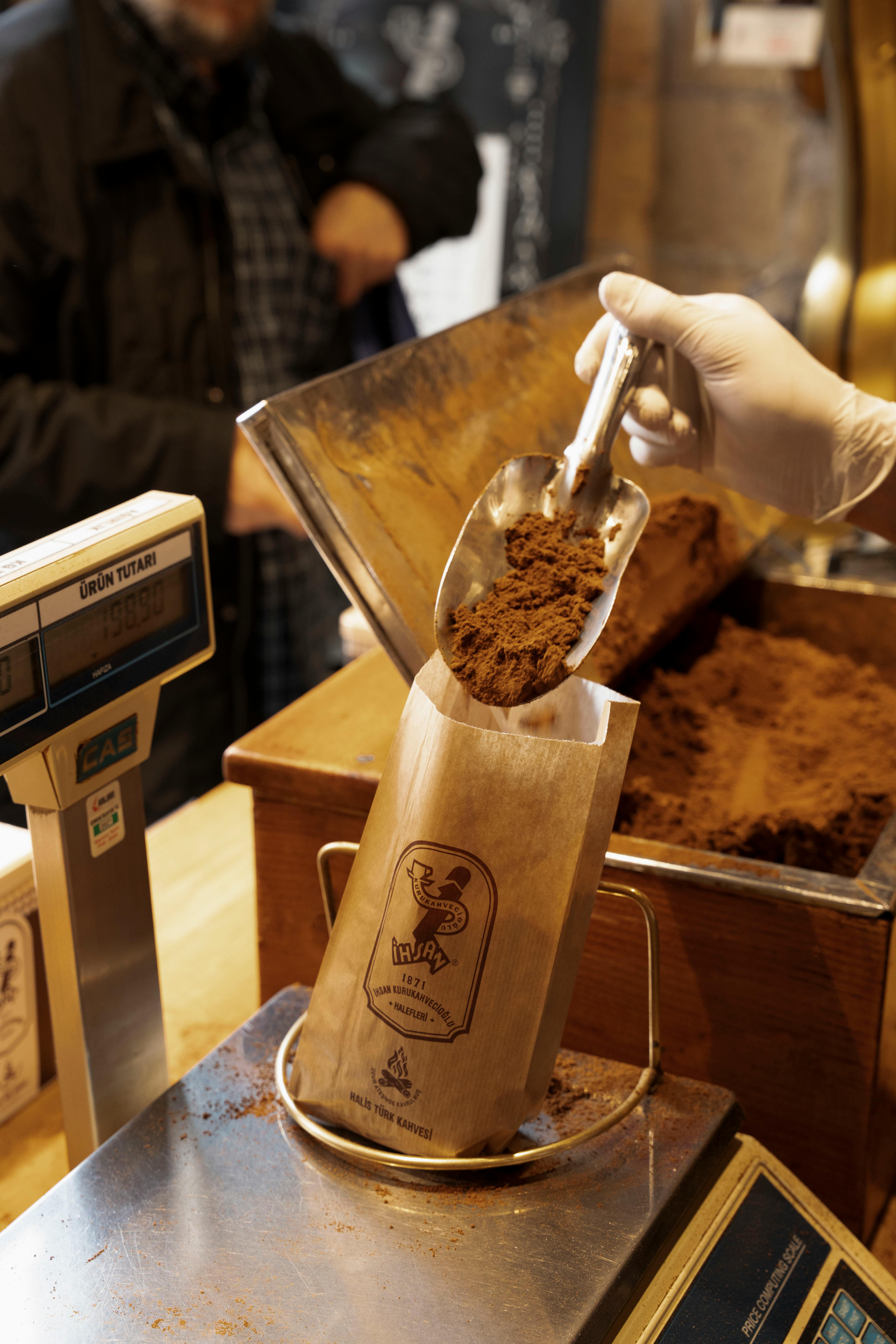 Hand scooping coffee powder into a paper bag at a local artisan shop counter.