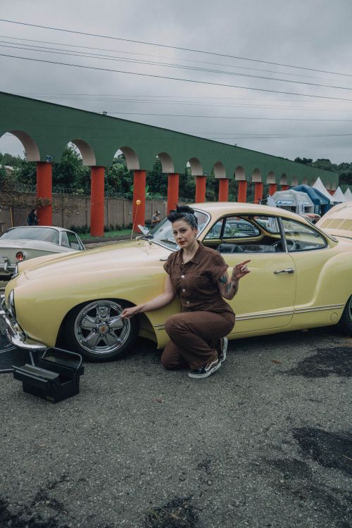 Free Woman poses with classic yellow car at outdoor auto show, showcasing unique vehicle design. Stock Photo