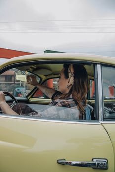 A stylish woman in a vintage car, embodying a retro 60s vibe, captured during the day.
