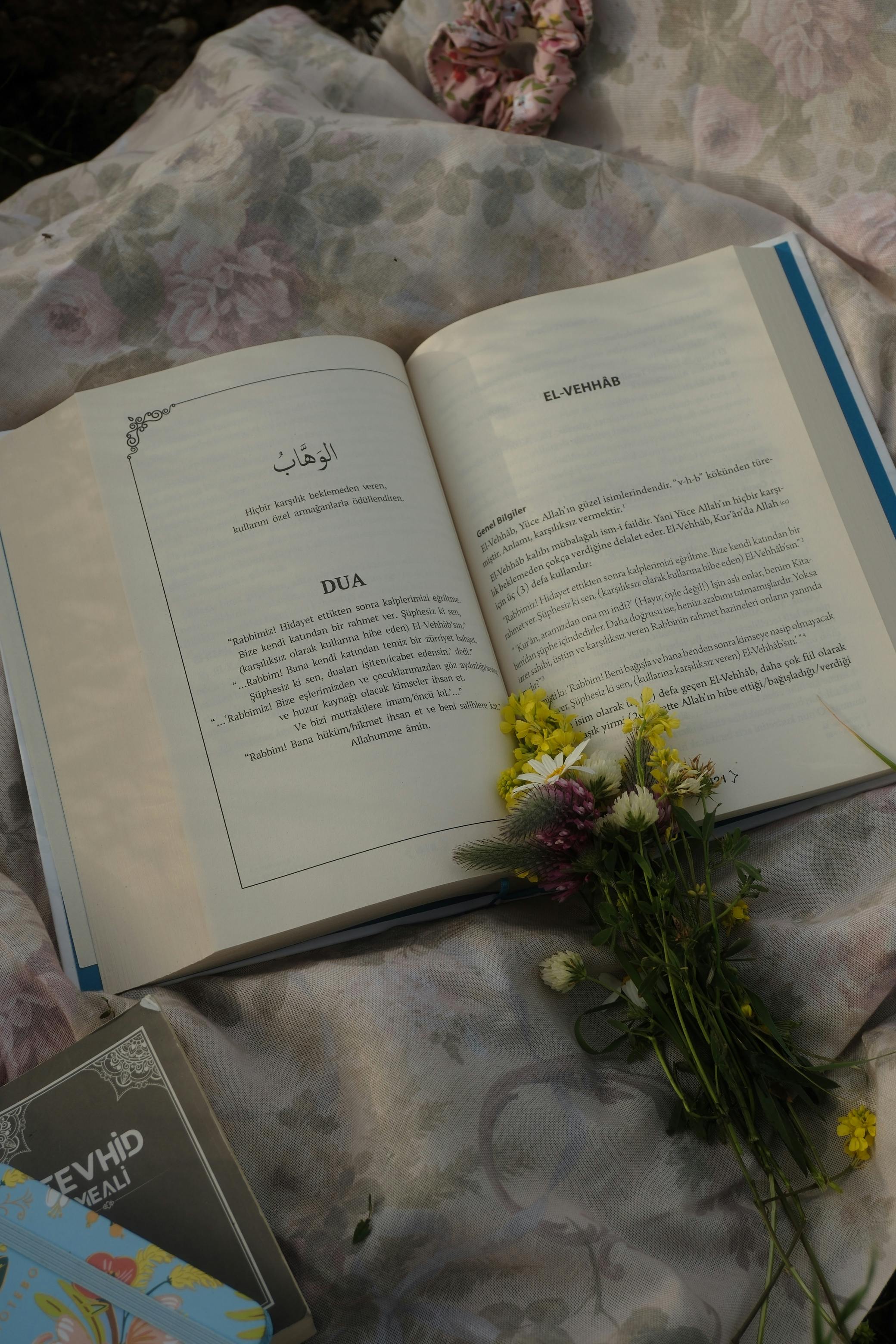 An open book with flowers elegantly placed on floral fabric, creating a serene and thoughtful composition.