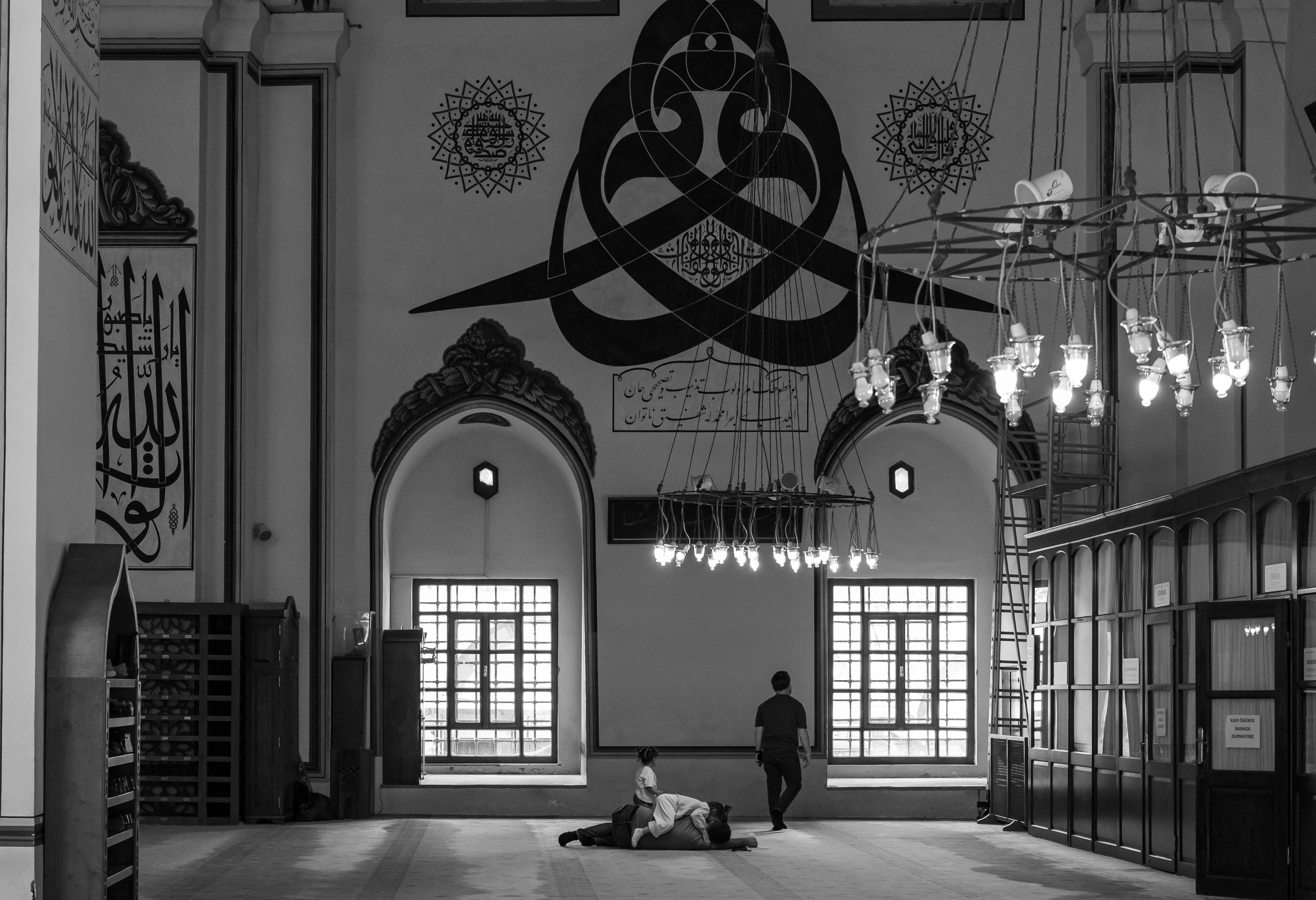 Monochrome image of a mosque interior featuring calligraphy and people, evoking a serene atmosphere.