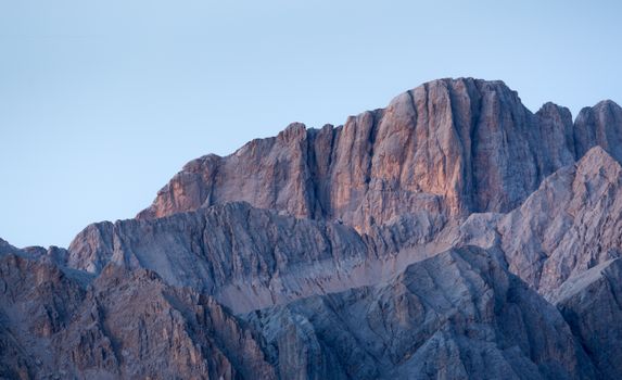 A stunning view of the Dolomites with warm lighting at sunset, showcasing rugged peaks and serene atmosphere.