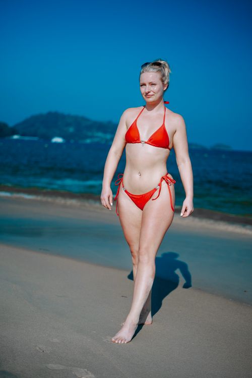 Free A woman in a red bikini enjoying a sunny day at a tropical beachfront within view of the ocean and distant hills. Stock Photo