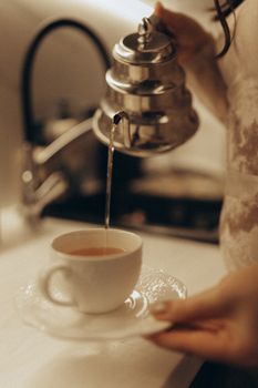 A person carefully pouring hot tea into a delicate teacup, creating a warm ambiance.