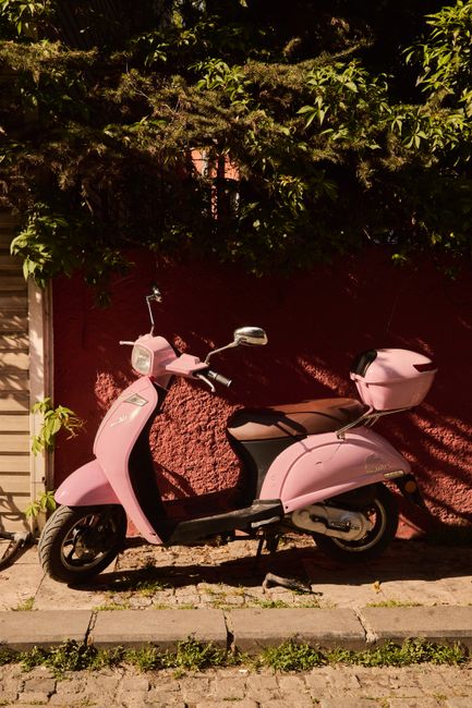 A vibrant pink scooter under warm sunlight against a rustic red brick wall.