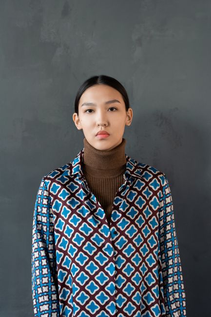 Fashionable portrait of a woman wearing a geometric patterned shirt and turtleneck against a grey ba