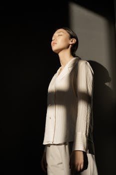 一位时尚女性闭眼倚墙而立，沐浴在阳光与阴影之中