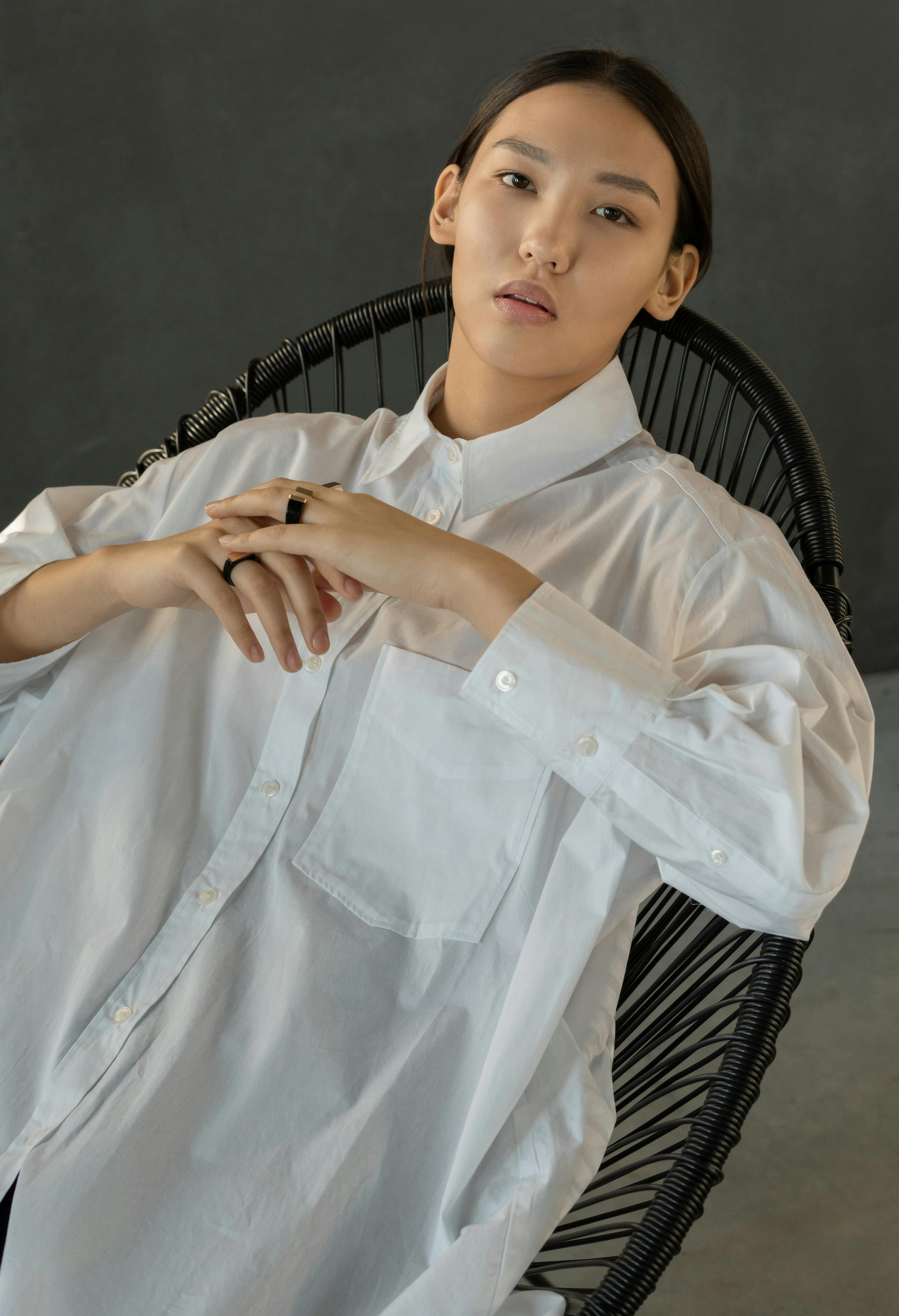 一位时尚女性身着白衬衫，在工作室中摆出轻松姿势的极简主义肖像