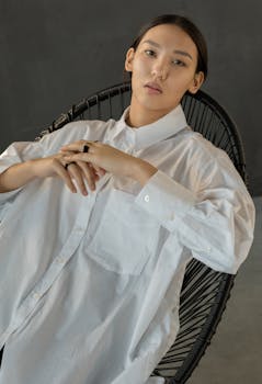 一位时尚女性身着白衬衫，在工作室中摆出轻松姿势的极简主义肖像