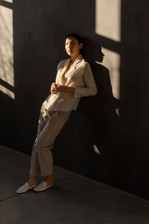 Free A stylish woman leaning against a wall, captured in moody lighting, conveying fashion elegance. Stock Photo