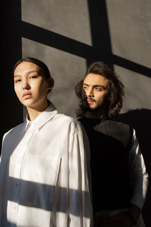 Free A fashionable couple stands in strong shadow lighting indoors, showcasing modern elegance. Stock Photo