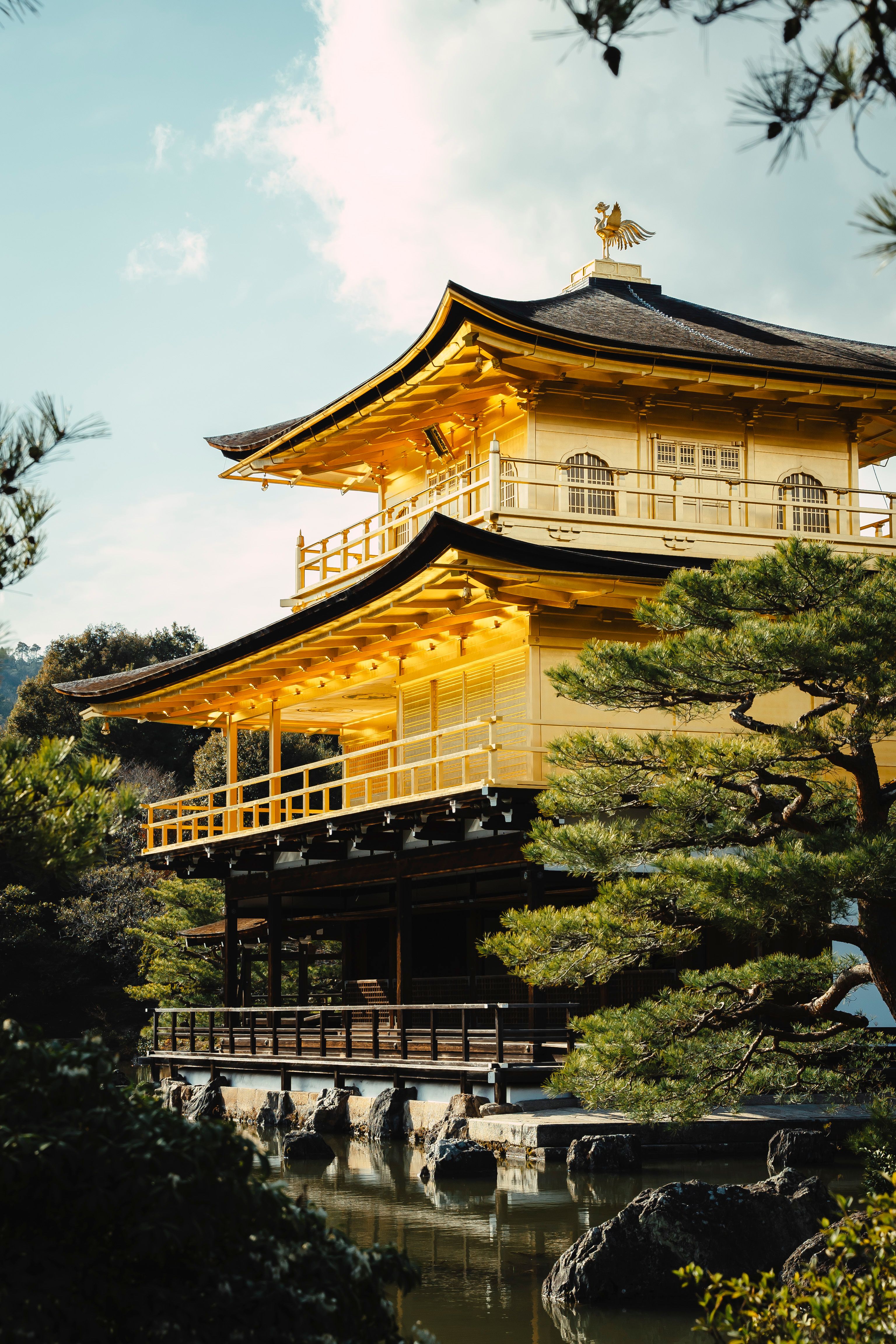 Photograph of the Golden Pavilion in Kyoto surrounded by lush greenery under a bright sky.