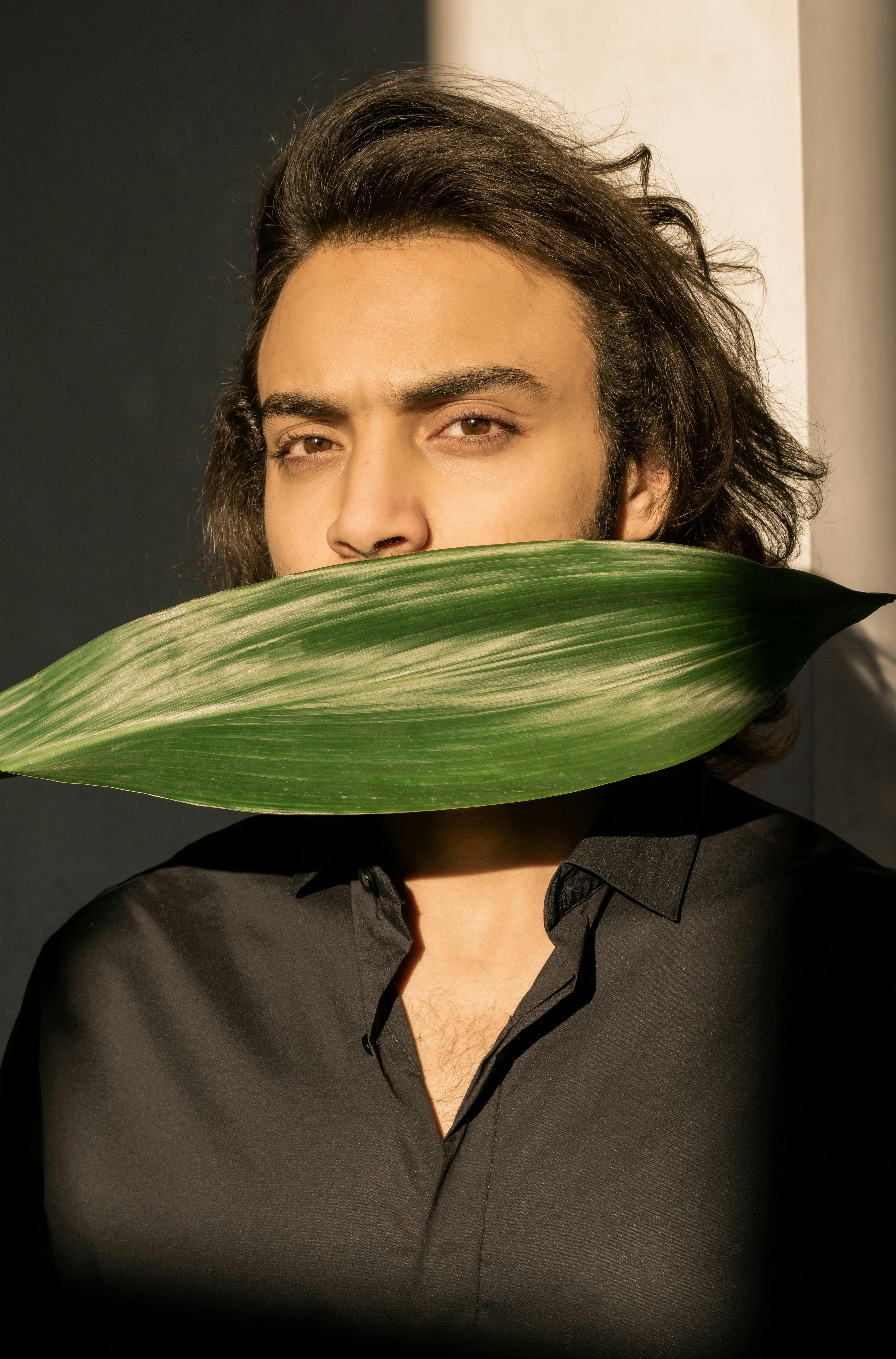 这幅肖像引人注目，描绘了一位部分被绿叶遮住的男人，巧妙地融合了自然与时尚