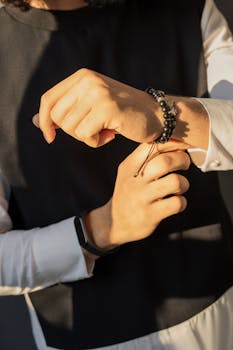 Close-up of hands adjusting a beaded bracelet in warm sunlight, showcasing elegance and style.