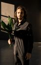 一名时尚男子手持绿色植物在室内，光影交错，构成了一幅富有戏剧性与艺术感的肖像