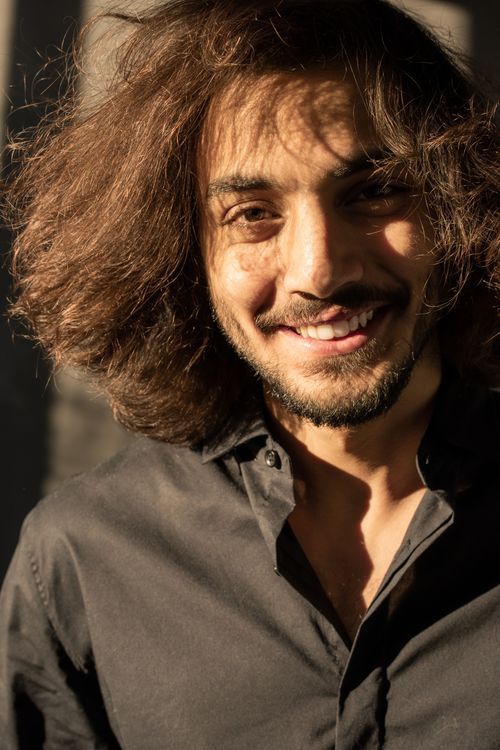 Free A cheerful man with wavy hair smiles warmly in bright sunlight. Stock Photo