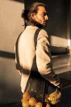 温暖的室内阳光下，一位时尚男子背着装有水果的网袋