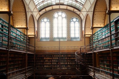 Free High-ceiling library with shelves of books and a spiral staircase, featuring large arched windows. Stock Photo